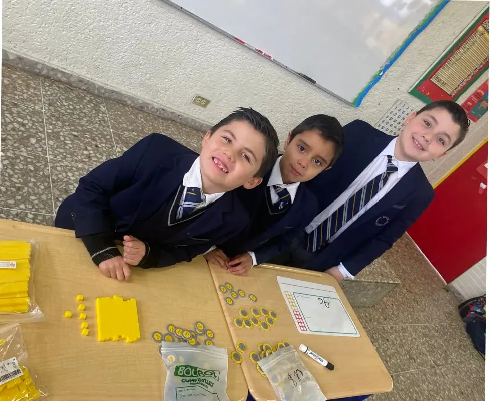 Estudiantes en uniforme escolar realizando una actividad colaborativa de dibujo y pintura en el aula con materiales creativos.